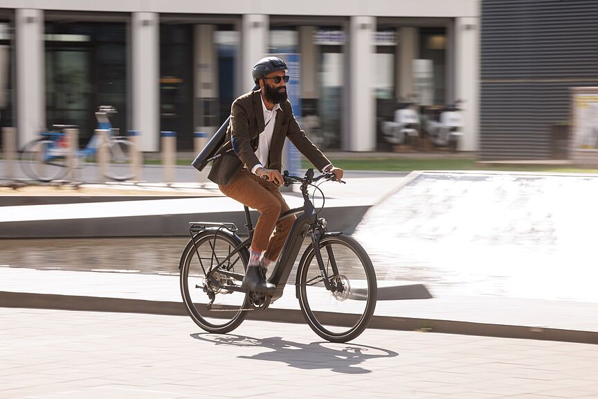 Urbane Mobilität: Geschäftsmann auf einem Elektrofahrrad in der Stadt Ein Pendler fährt auf seinem elektrischen Fahrrad durch das Stadtgebiet.